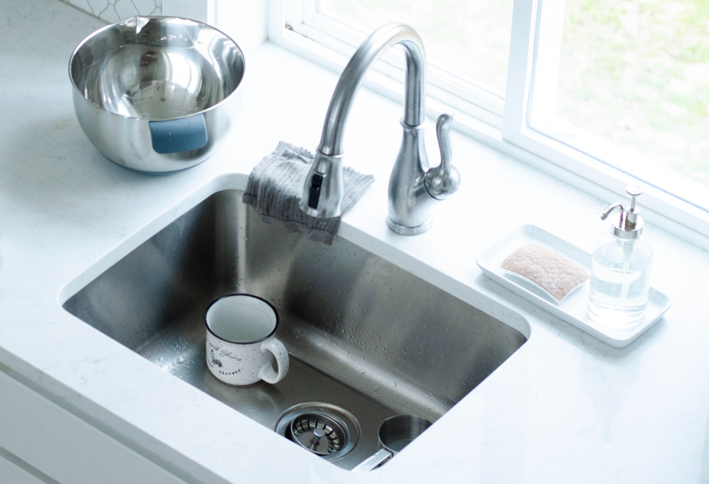 Image of a chrome sink with a white mug inside. A metal bowl is on the counter beside the sink.