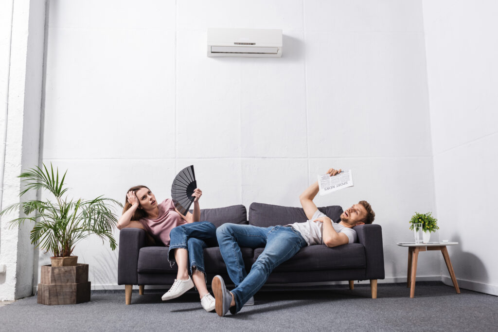 young couple fanning themselves while suffering from heat at home with broken air conditioner