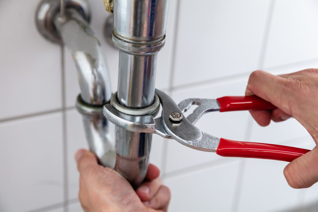 Close-up of a plumber's hands repairing a sink's pipes with an adjustable wrench.