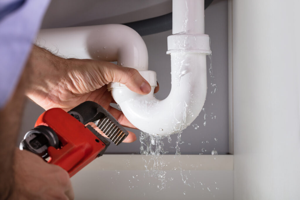 Close-up image of a plumber fixing a drain with a wrench.