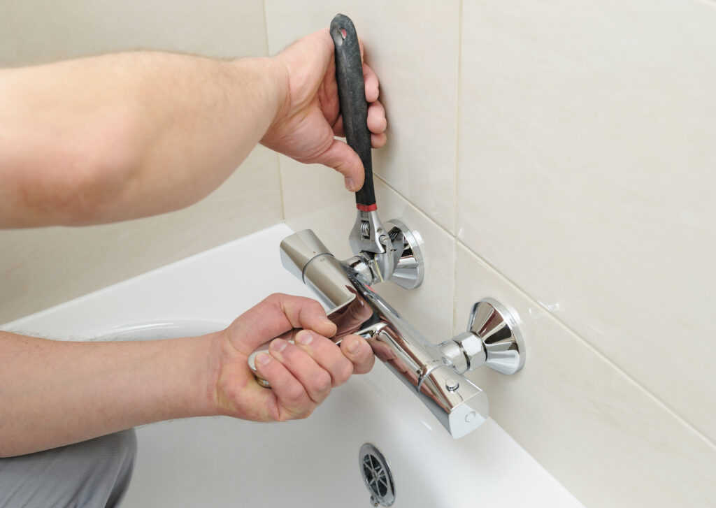 A person installing a bath faucet with a wrench