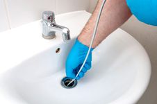 Person wearing a blue glove, using a drain-cleaning tool to unclog a sink.