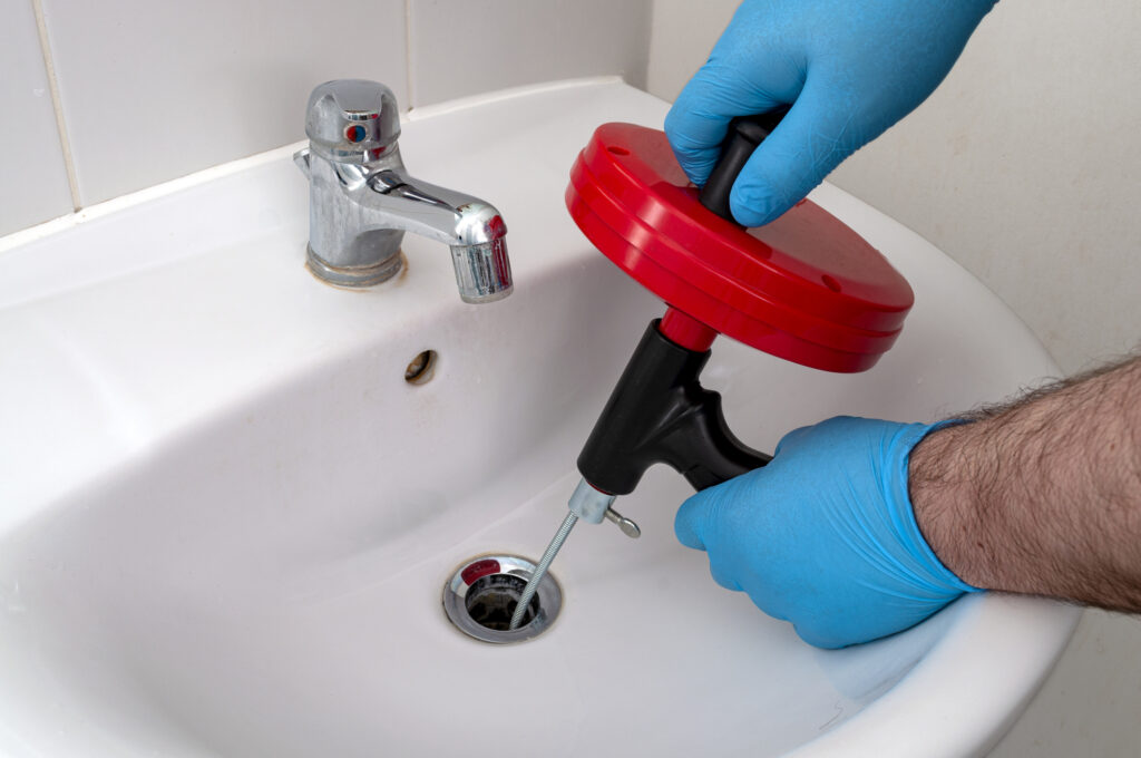 A technician using a drain snake on a bathroom sink