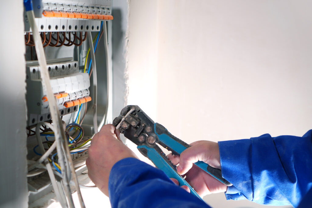 Electrician works with an electrical switchboard with automats and wires.