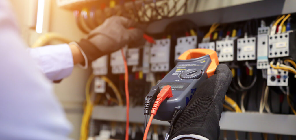 Electrical engineer using digital multi-meter to check current voltage at circuit breaker in main distribution board.