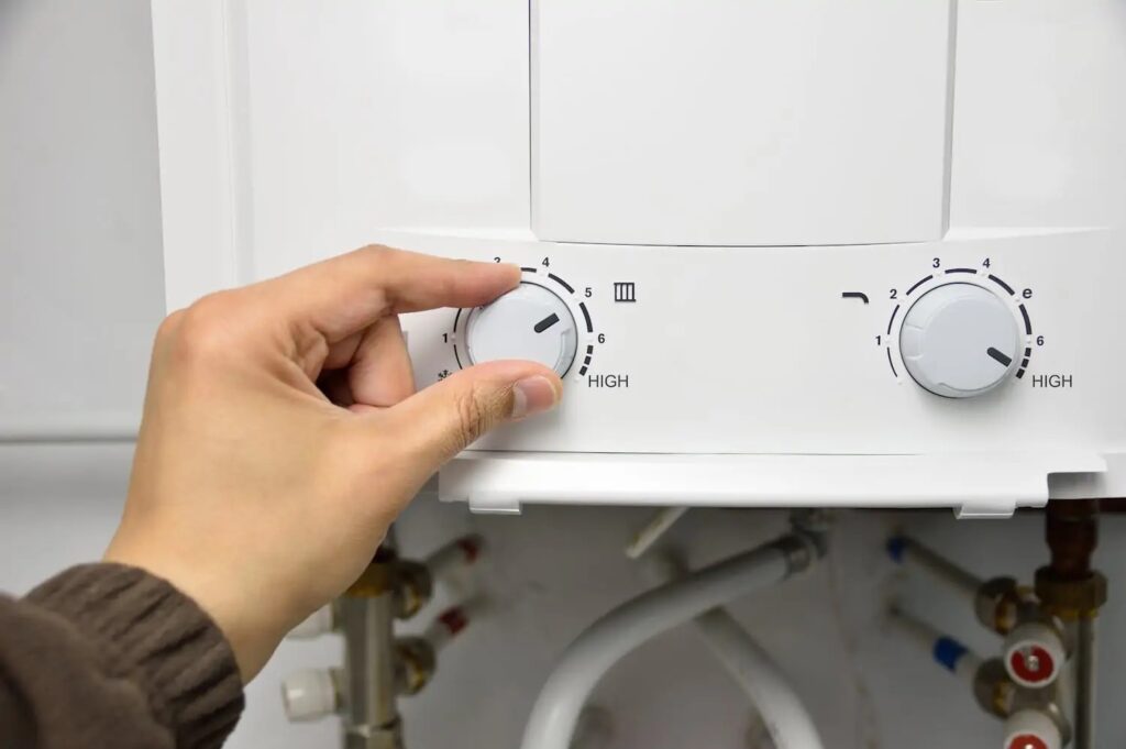 A hand is adjusting a turn dial on a white tankless water heater