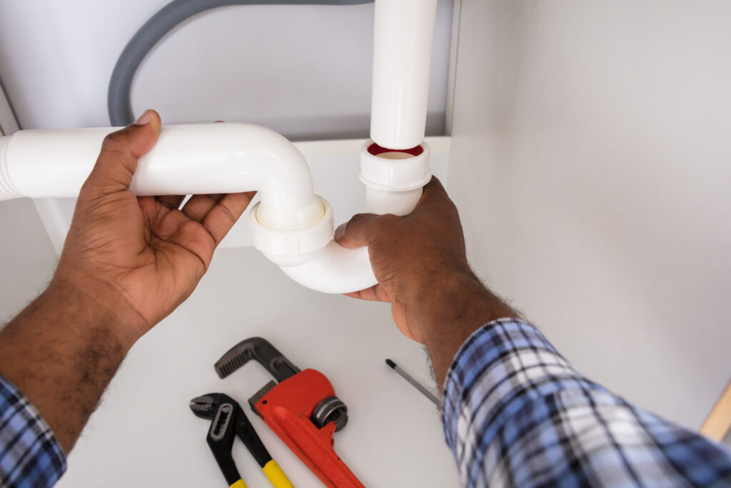 Close-up of plumber fitting sink pipe in kitchen at home