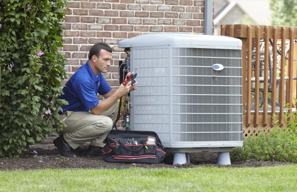 An HVAC technician is kneeling next to an outdoor AC unit for a tune-up.