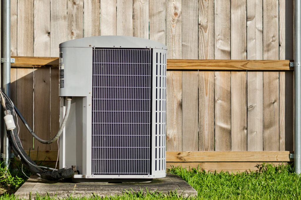 Central air conditioning unit in a residential backyard in front of a wooden fence