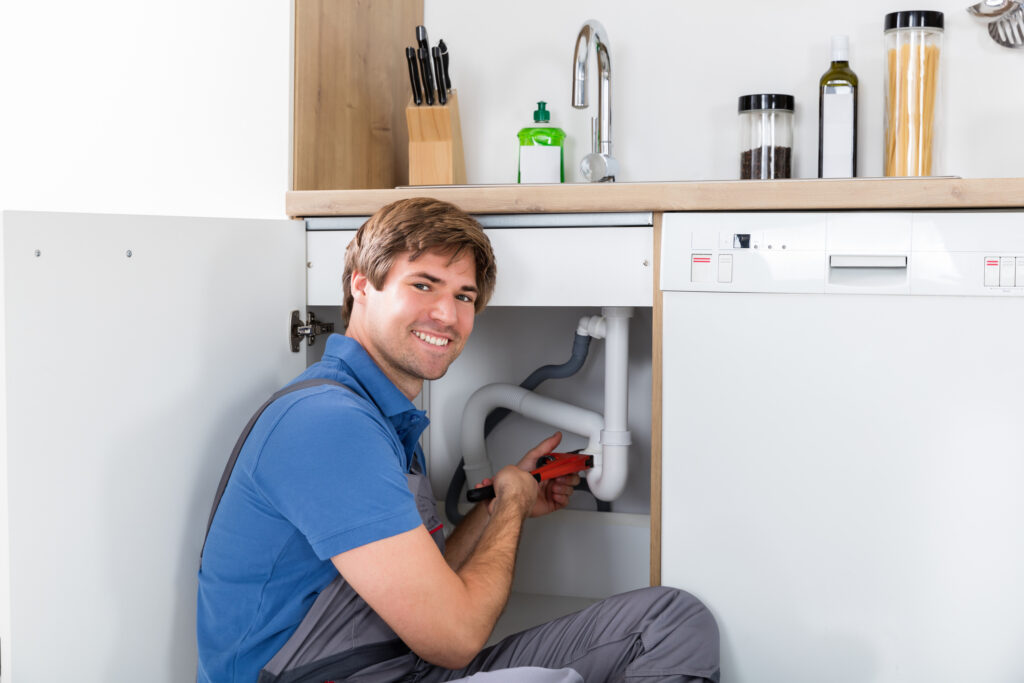 Plumber fixing sink pipe with adjustable wrench in kitchen