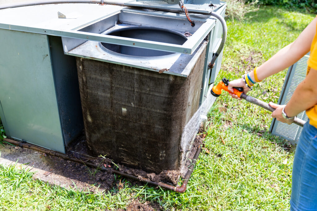 Person using hose to clean dirty condenser coils on an air conditioner system