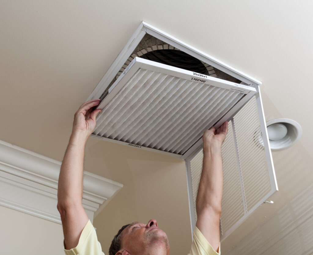 A person reaching up to open the filter holder for air conditioning filter in ceiling